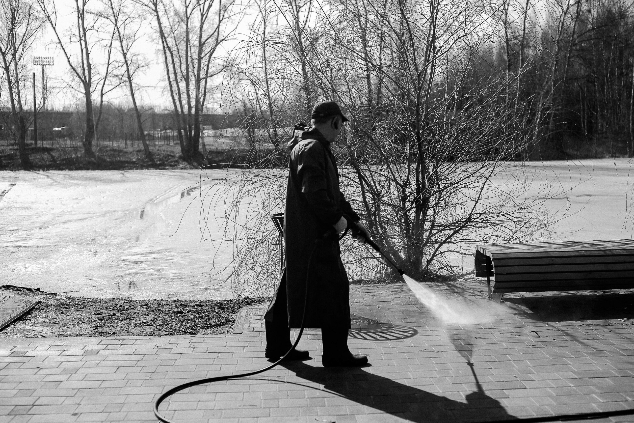 A man pressure washing pavement in a winter landscape captured in black and white.