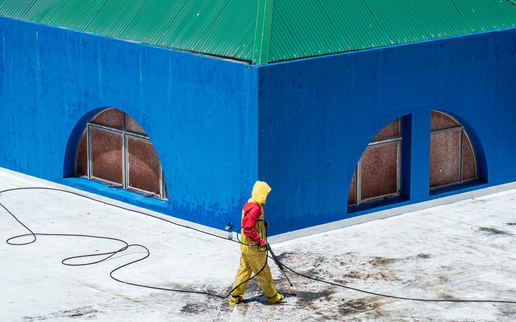 A worker in protective gear power washes a vibrant blue building exterior.